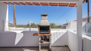 An outdoor barbecue grill with a chimney, a tiled patio, and a white wall.