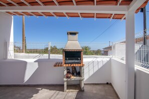 Una parrilla para barbacoa al aire libre con chimenea, un patio con baldosas y una pared blanca.