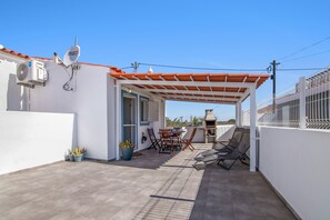 A covered patio with a table and chairs, a barbecue grill, and a satellite dish.