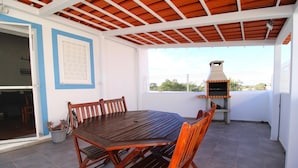 Une terrasse extérieure avec une table et des chaises en bois, un barbecue et une vue sur le ciel.
