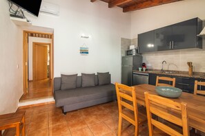 A compact kitchen with a grey sofa, wooden dining table, and a microwave.
