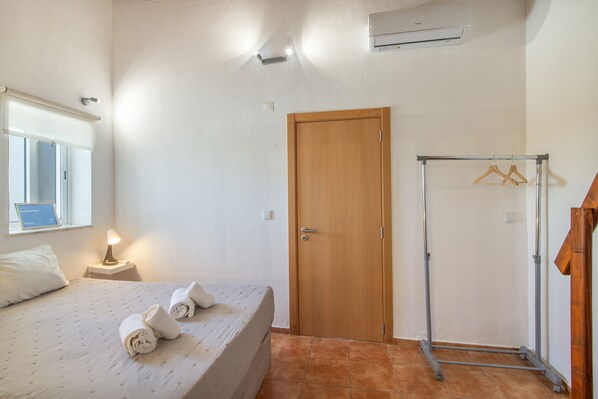 Un dormitorio con una cama, una puerta de madera, un perchero y una ventana.