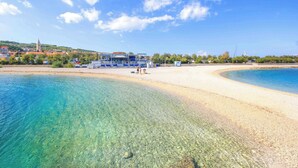 A beach with clear water, a sandy shore, and a building with a blue roof. - A1 Spacious apartment with terrace, 1 min walking to the beach (Supetar)