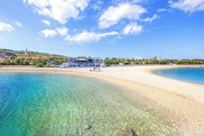 Une plage avec une eau cristalline, un rivage sablonneux et un bâtiment surmonté d’un toit bleu.