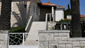 A stone building with a tiled roof, a staircase, and palm trees. - A1 Spacious apartment with terrace, 1 min walking to the beach (Supetar)