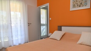 A bedroom with an orange wall, a bed with white pillows, a door with a mirror, and a window with blinds. - A1 Spacious apartment with terrace, 1 min walking to the beach (Supetar)