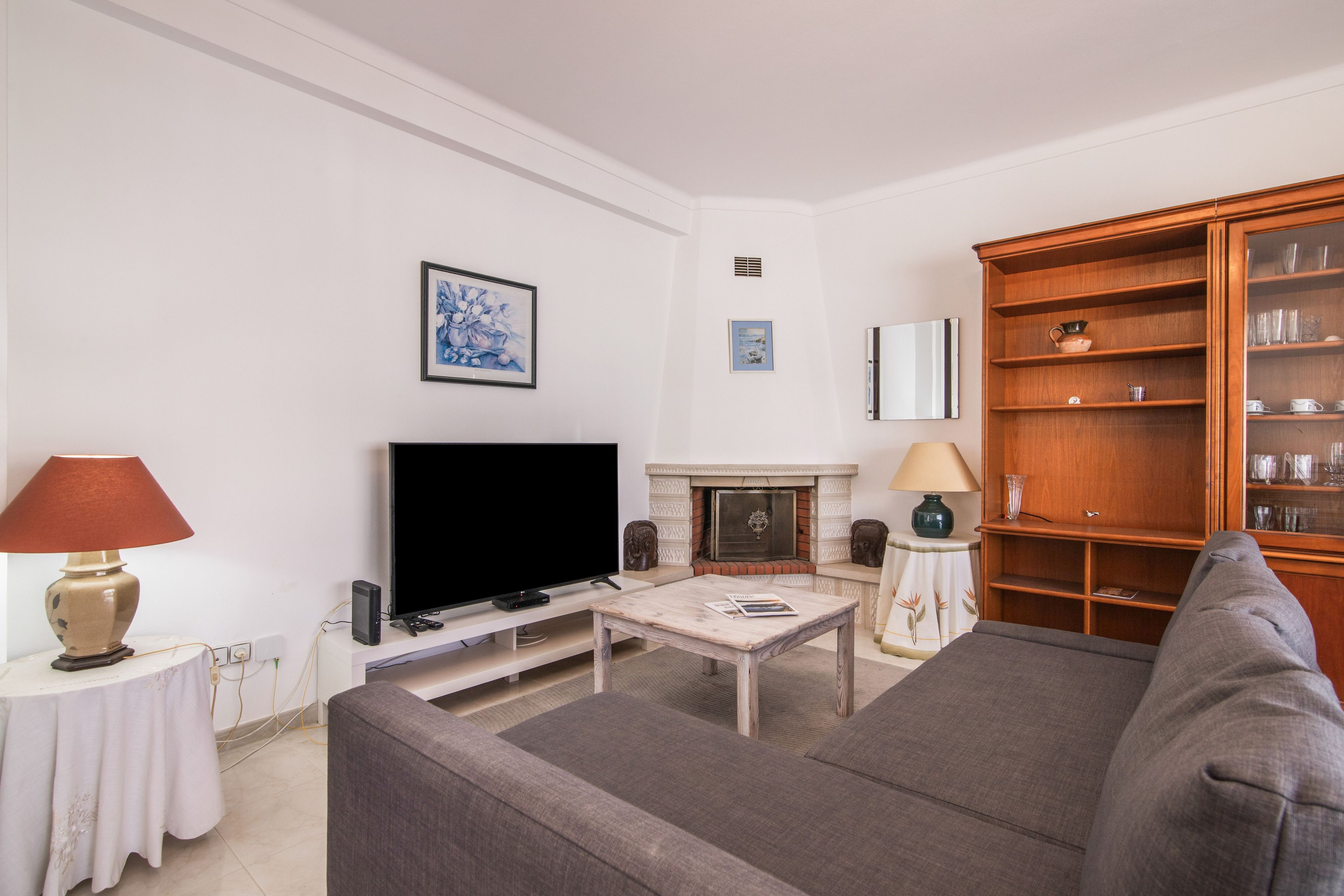 Een woonkamer met een flatscreen televisie, een open haard, een houten kast en een bank.