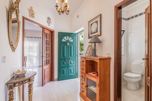 A hallway with a green door, a wooden cabinet, a mirror, and a chandelier.