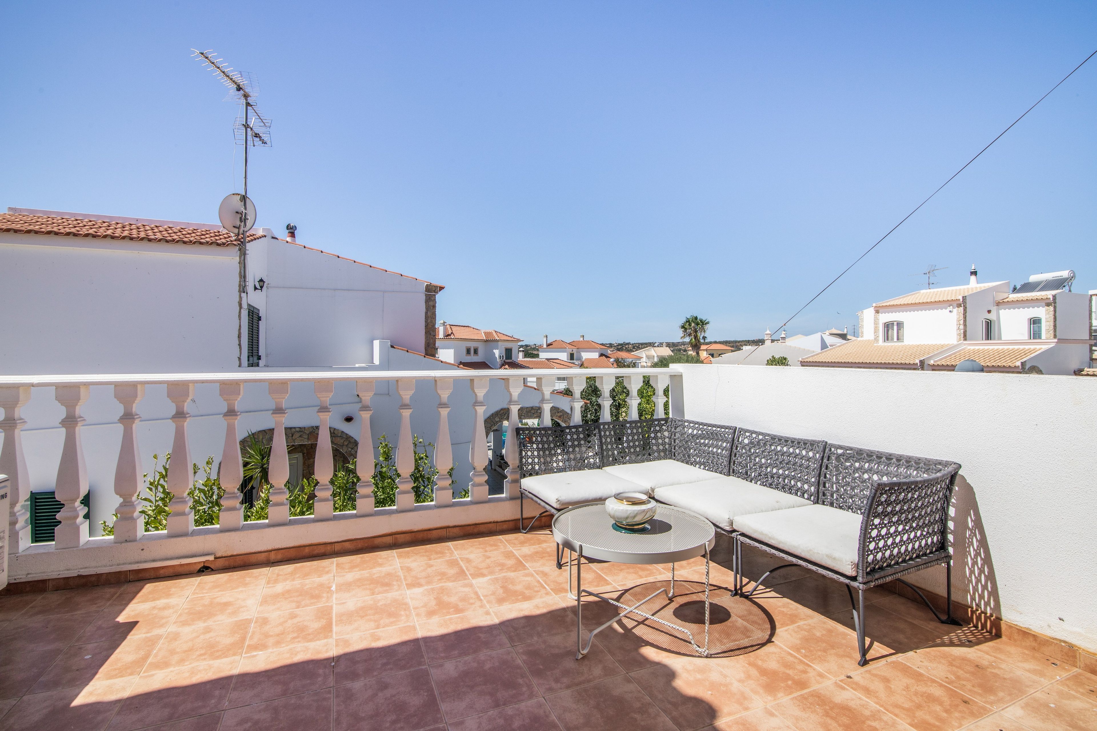 Una terraza con un sofá blanco, una mesa redonda y una cerca decorativa.