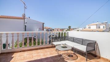 Una terraza con un sofá blanco, una mesa redonda y una cerca decorativa.