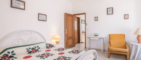Un dormitorio con cama, una silla, una mesa y una puerta.