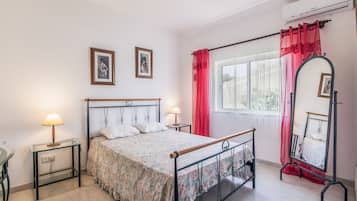 A bedroom with a bed, two bedside tables, a mirror, and a window with curtains.