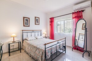 A bedroom with a bed, two bedside tables, a mirror, and a window with curtains.
