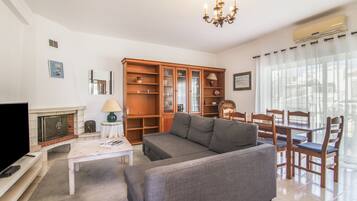 Una sala de estar con sofá, televisión, chimenea, mueble de madera y mesa de comedor.