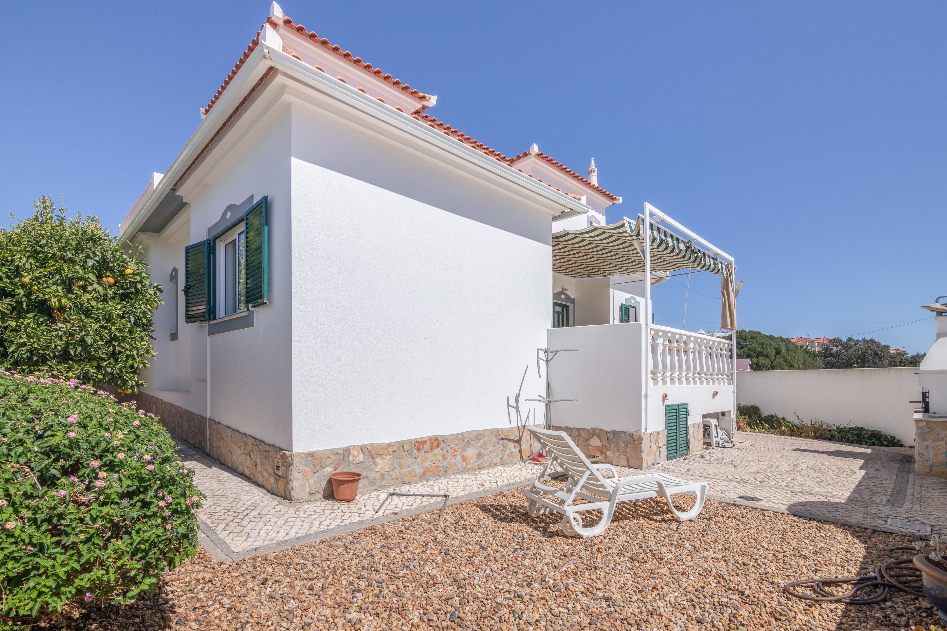 A white building with a tiled roof, a balcony with a white railing, and a gravel driveway.