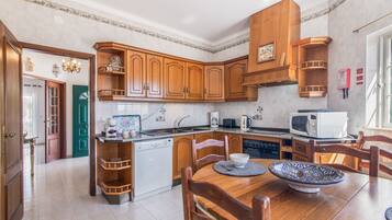 Una cocina con armarios de madera, una mesa de comedor con sillas, un microondas y una cafetera.