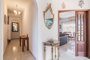 A hallway with a mirror, a small table with decorative items, and a door leading to a living area.