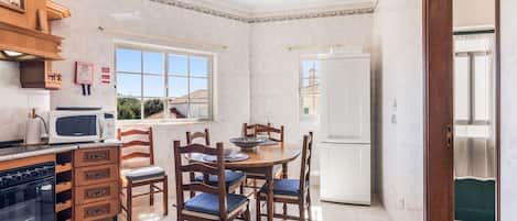 A compact kitchen with a dining area, featuring a microwave, stove, cabinets, and a refrigerator.