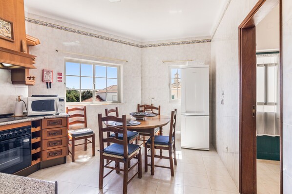 A compact kitchen with a dining area, featuring a microwave, stove, cabinets, and a refrigerator.