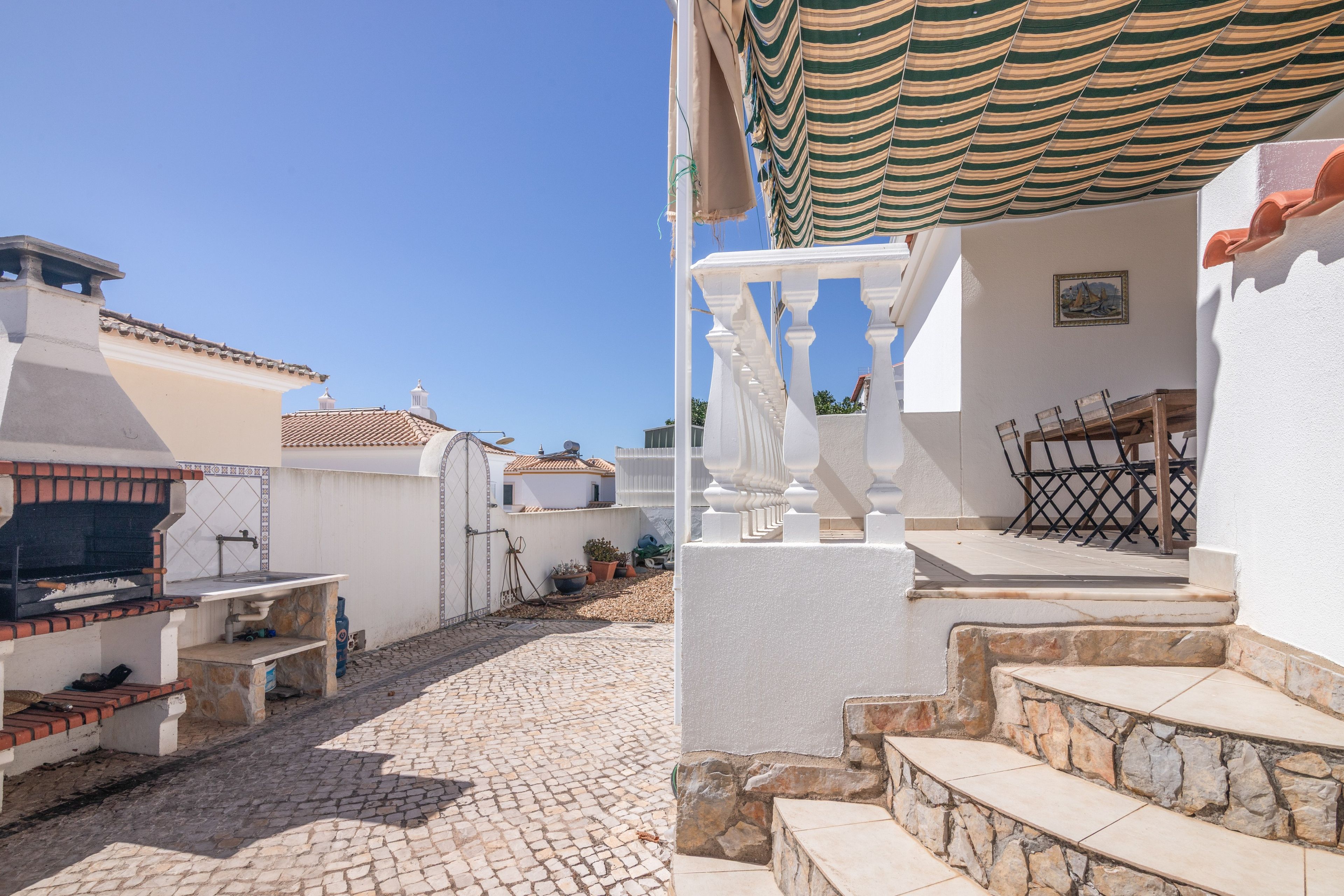 Un patio con suelo de piedra, una parrilla de barbacoa y una escalera blanca que conduce a una zona cubierta.