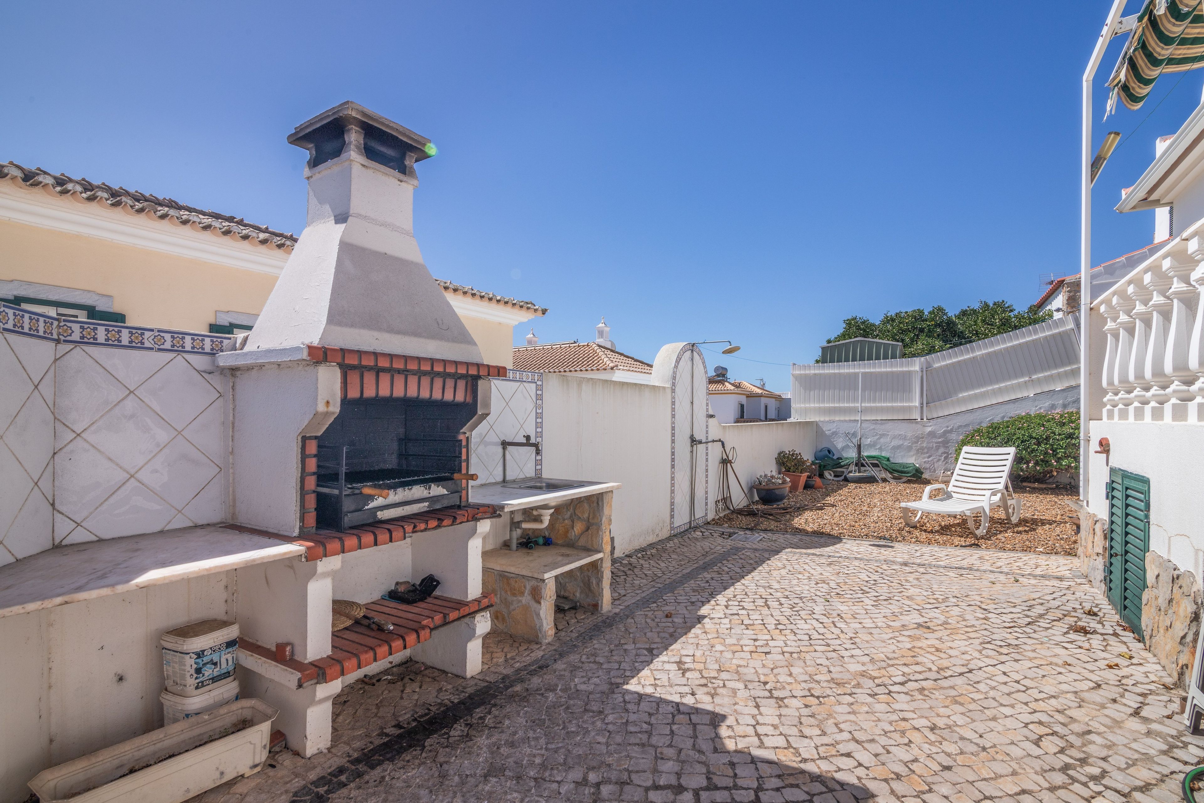 Un patio con una parrilla, piso de baldosas de piedra y pared blanca adornada con una banda de azulejos decorativos.