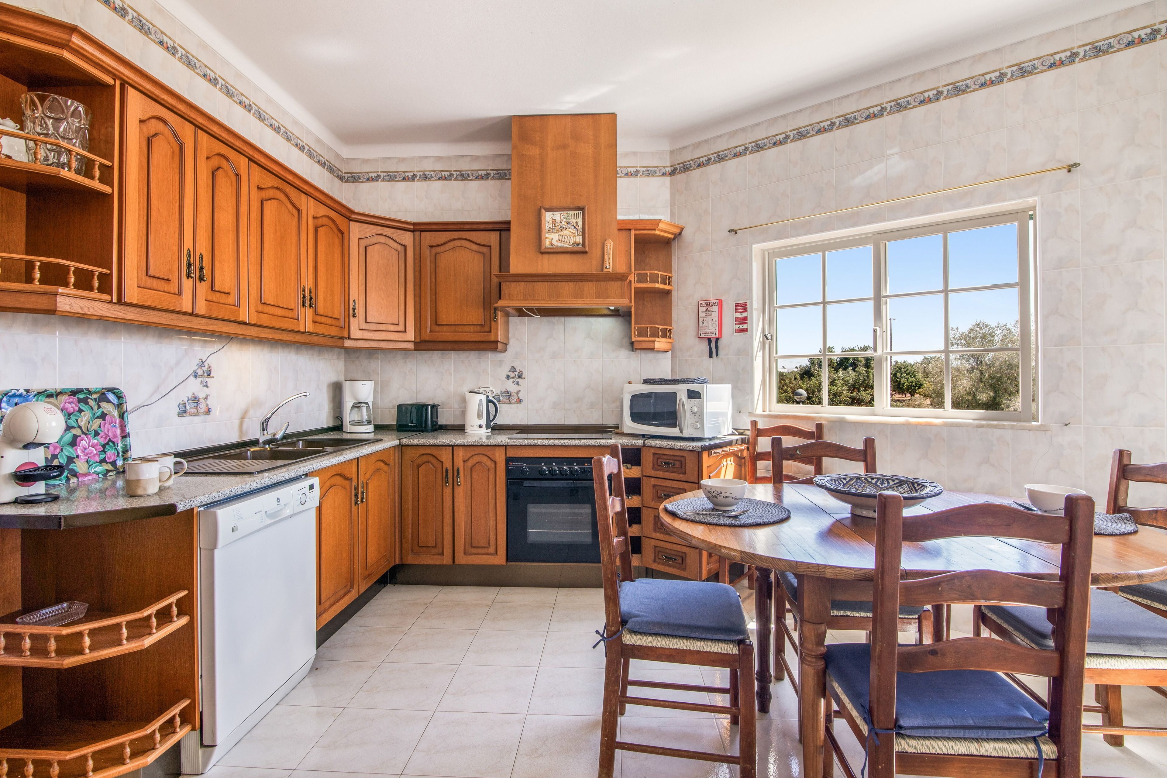 Una cocina con armarios de madera, lavavajillas, microondas y una mesa de comedor con sillas.