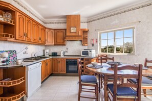 Una cocina con armarios de madera, lavavajillas, microondas y una mesa de comedor con sillas.
