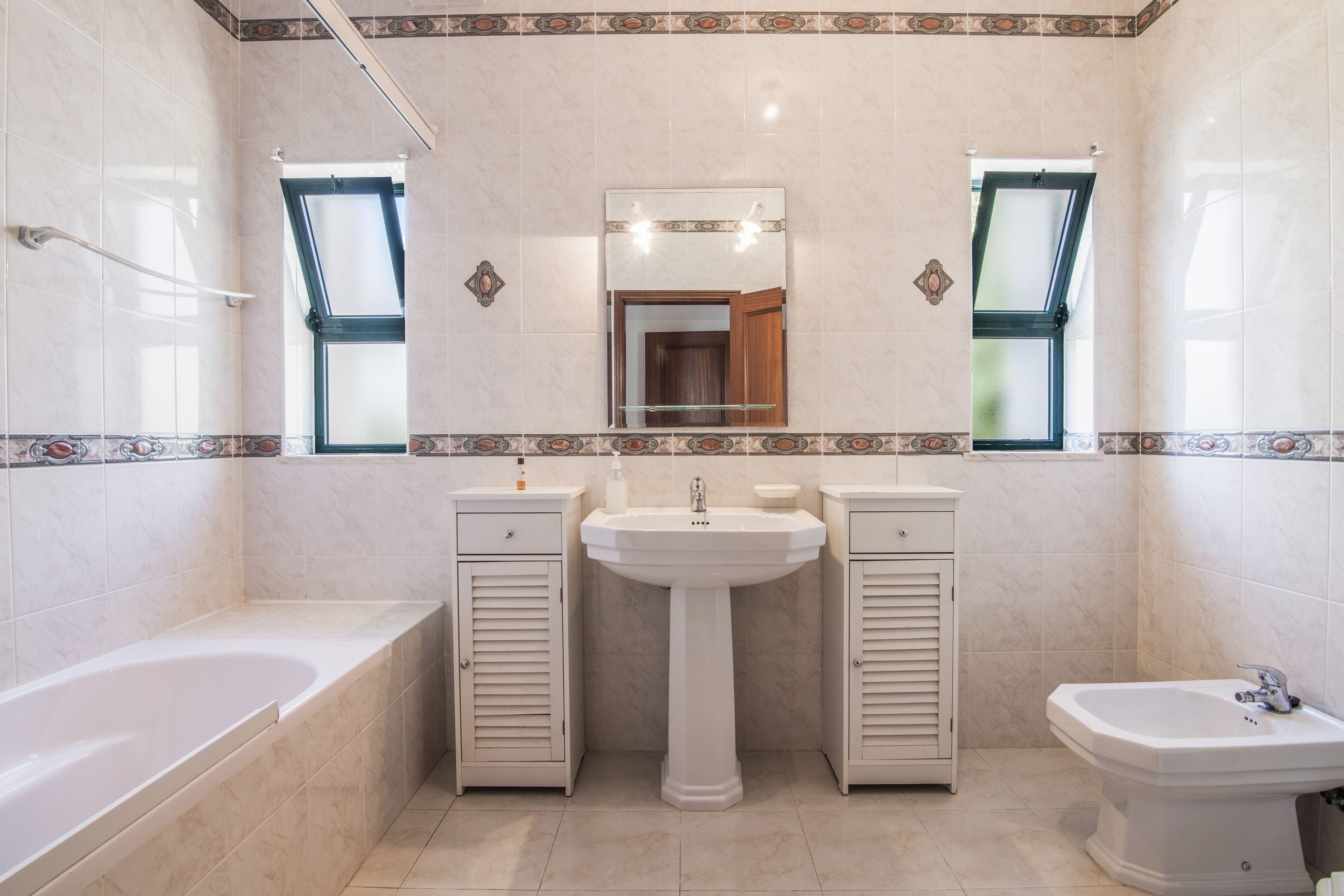 A bathroom with a bathtub, a sink, and a bidet. There are two vanity mirrors and a window above the sink.