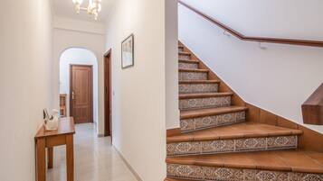 Un couloir avec une porte en bois, une petite table ornée d’un objet décoratif et un escalier dont les marches sont recouvertes de carreaux à motifs.