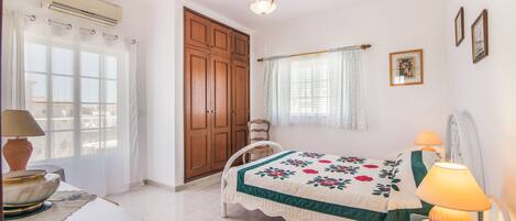 Un dormitorio con cama, escritorio, silla, armario, ventana con cortinas y una araña.