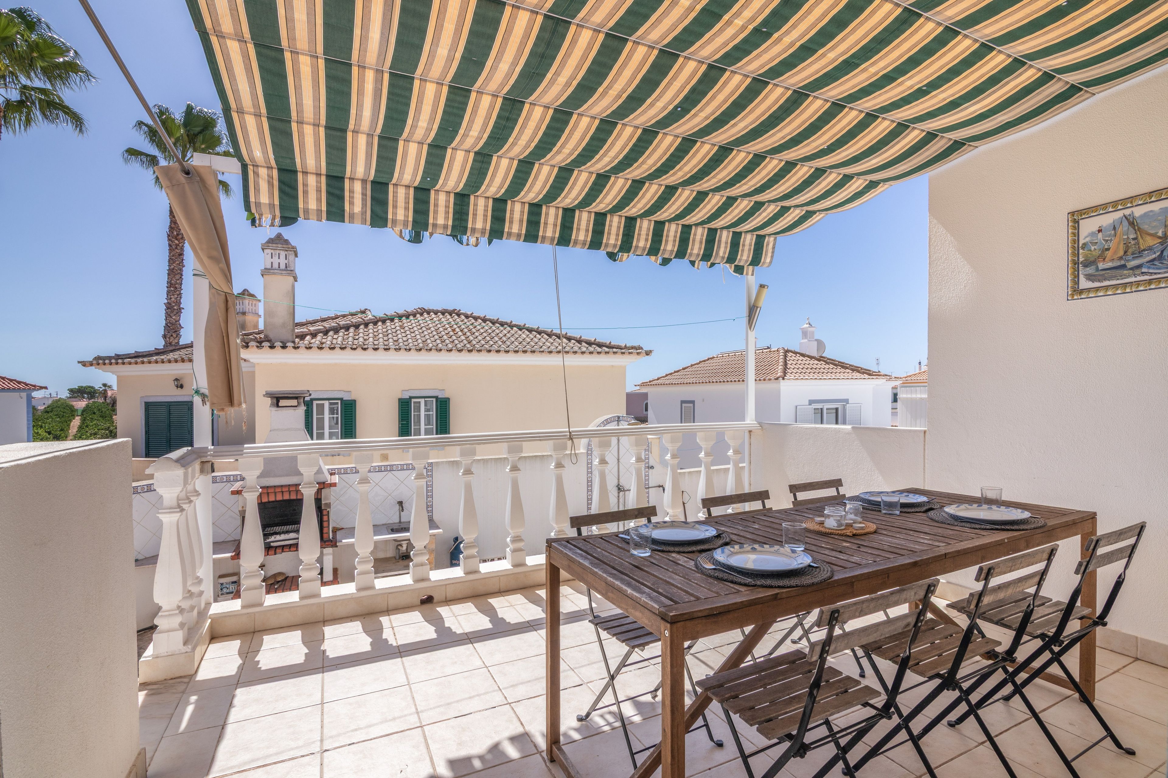 Eine Terrasse mit Esstisch, einem Streifen-Markisenvorzelt und Blick auf Häuser mit Ziegeldächern.