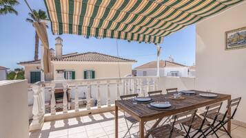 Eine Terrasse mit Esstisch, einem Streifen-Markisenvorzelt und Blick auf Häuser mit Ziegeldächern.