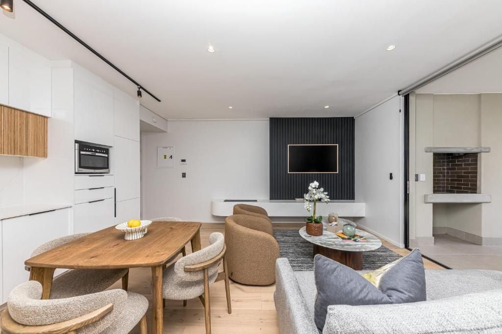 A modern kitchen with white cabinetry, a wooden dining table, and a flat-screen TV mounted on the wall.