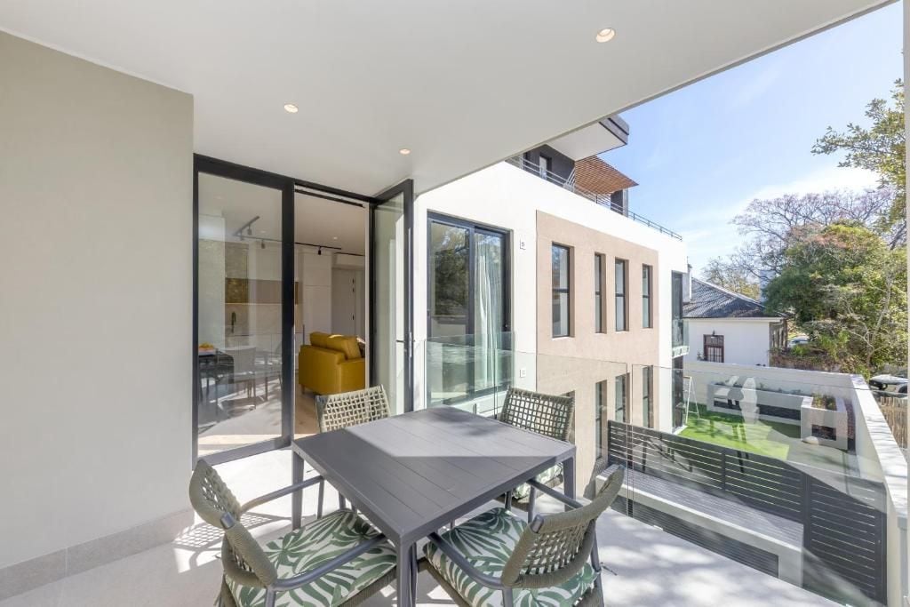 A modern outdoor dining area with a table and chairs, a glass door leading to a room, and a view of a residential building.
