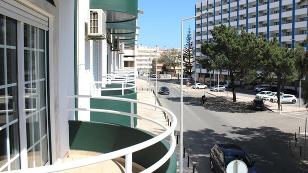 Un balcone d'hotel con vista su una strada, auto parcheggiate e un palazzo a più piani.
