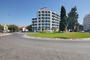Un edificio a più piani con facciata bianca e balconi verdi, situato presso una rotatoria con un'isola verde.
