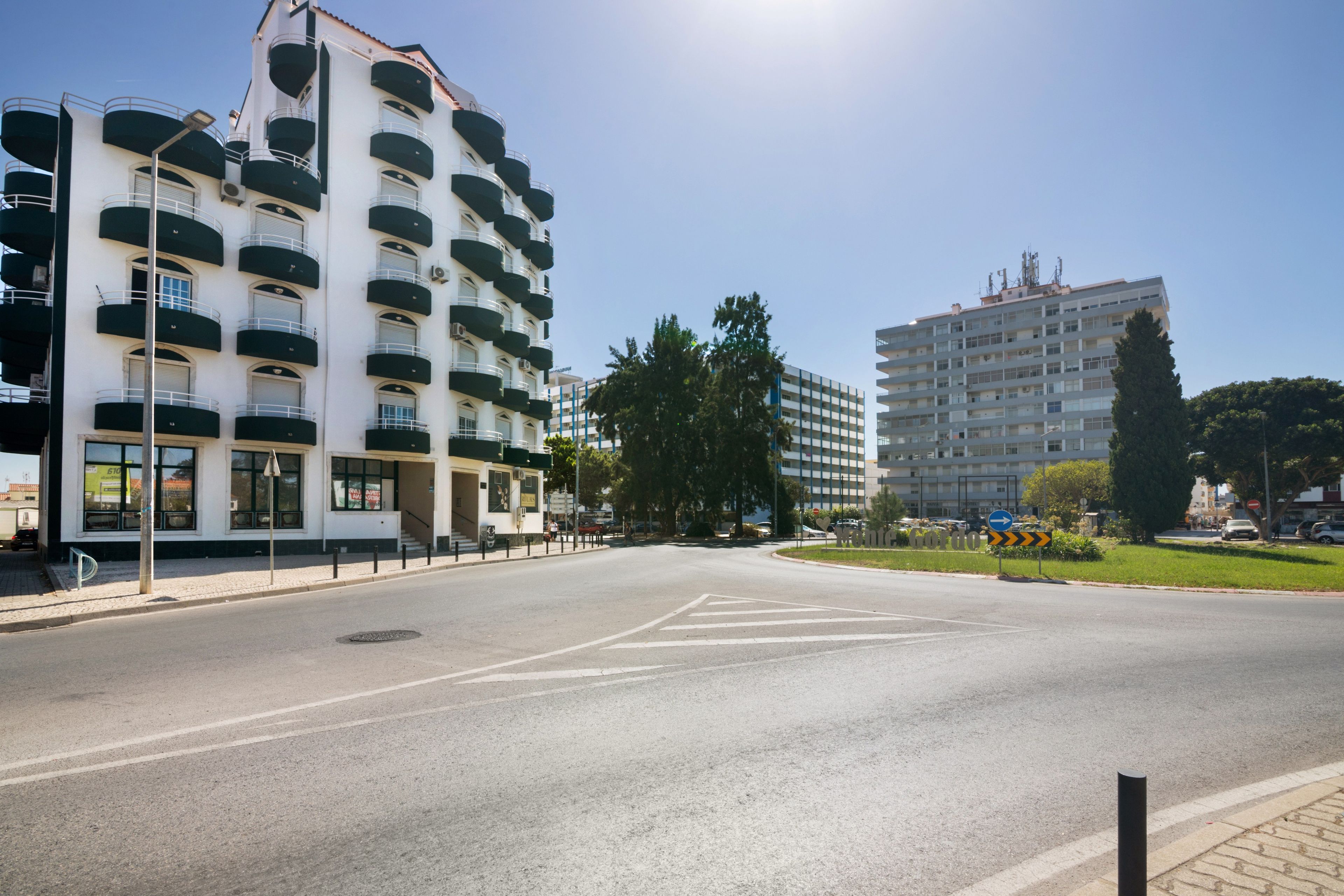 Un edificio de varios pisos con balcones, cielo despejado y una carretera con señales de tráfico.