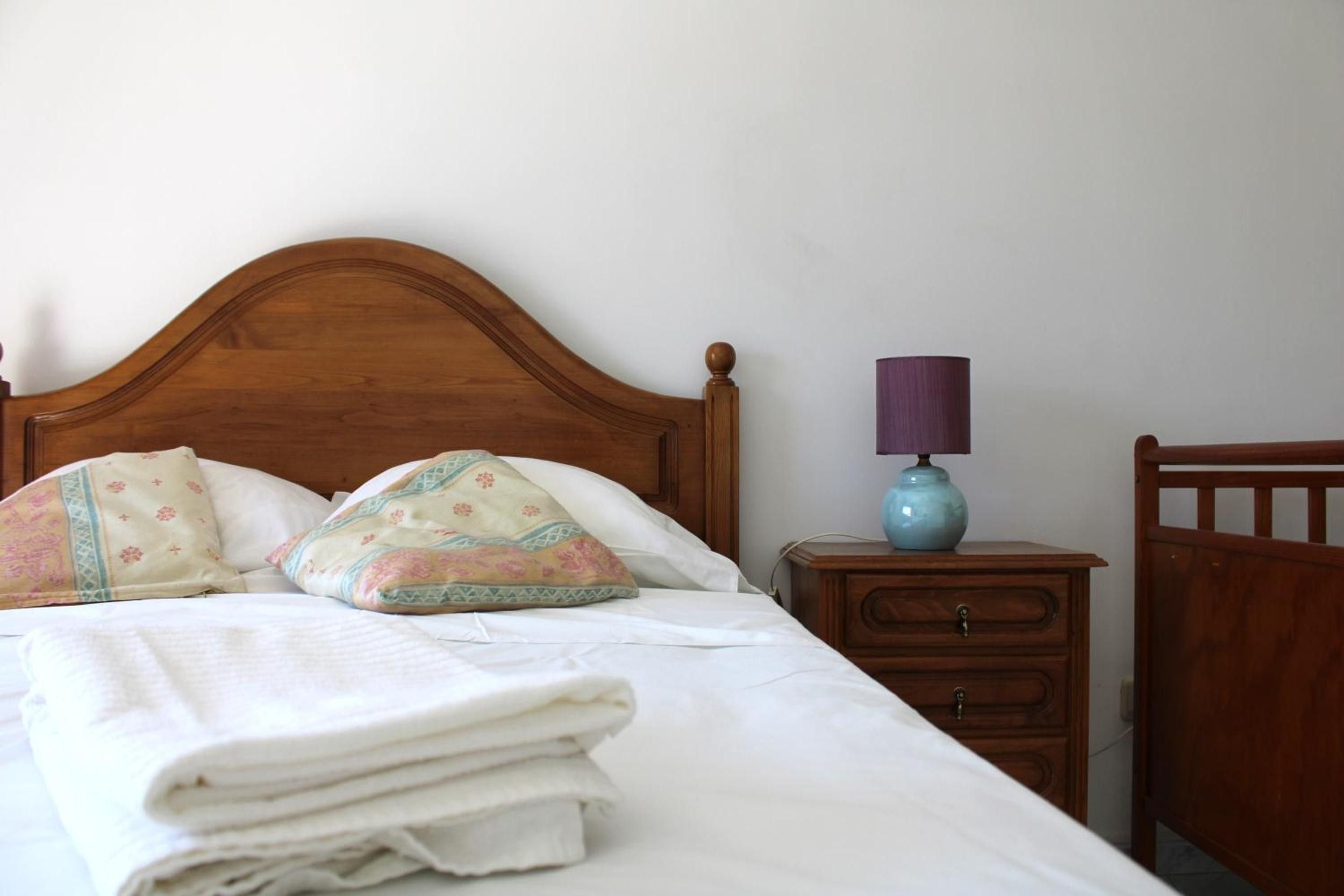 A neatly made bed with a wooden headboard, a bedside table with a lamp, and a nightstand with a drawer.