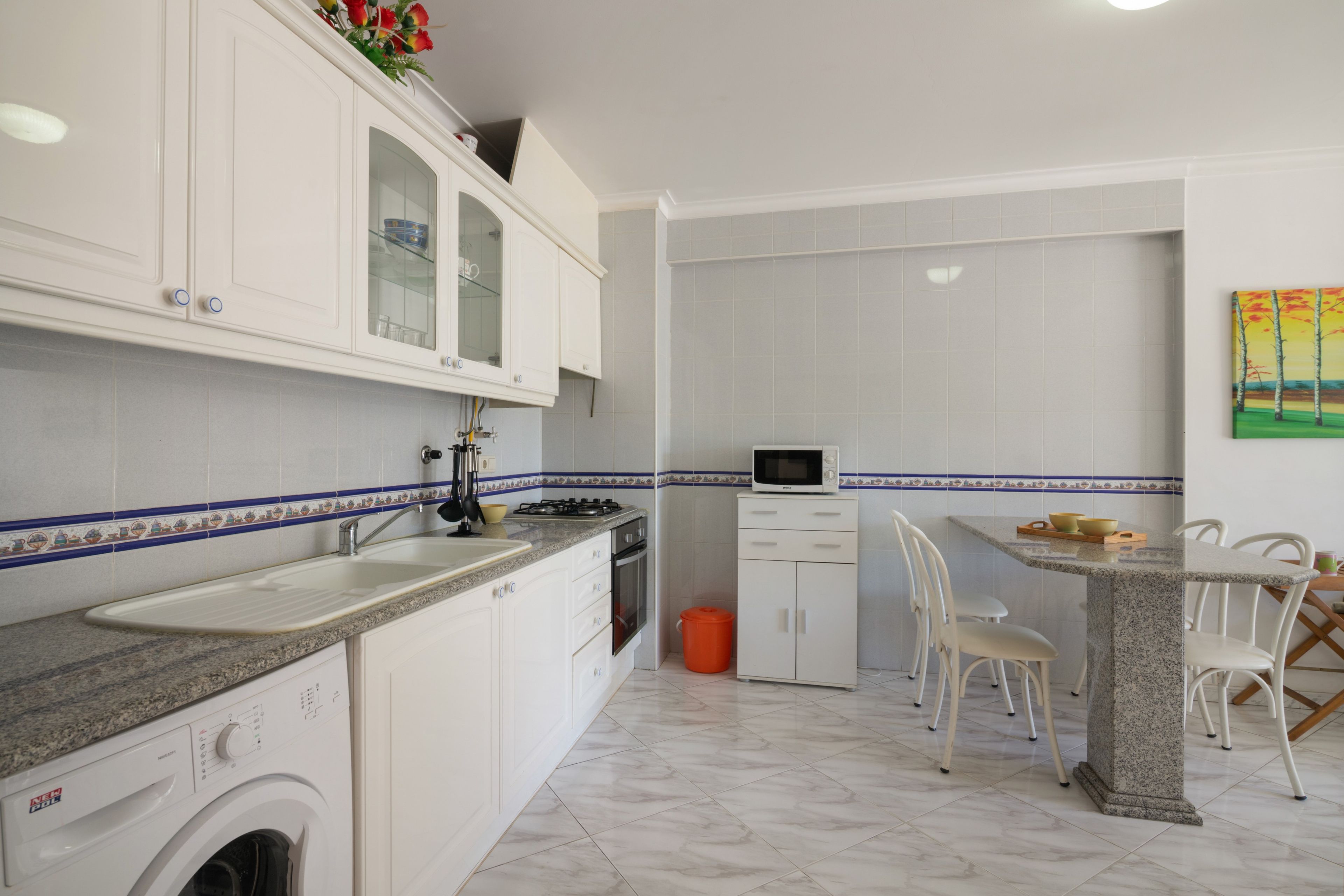 Een keuken met witte kastjes, een magnetron, een spoelbak en een wasmachine.