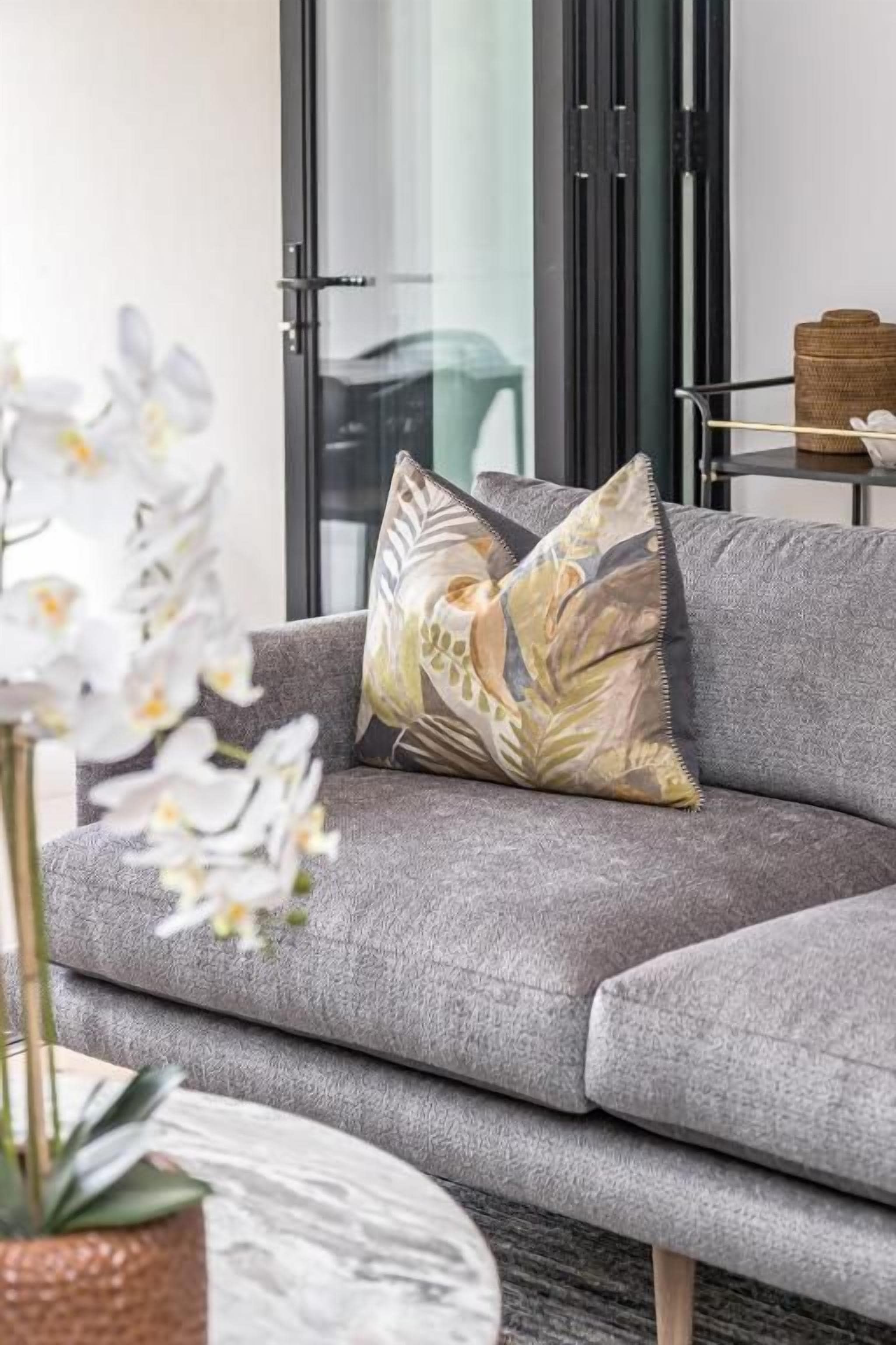 A grey sofa with a decorative pillow, a potted plant, and a wicker basket on a table.