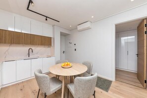 A modern kitchen with white cabinets, a marble backsplash, and a round wooden table with chairs. - Superior One-bedroom Garden - Unit 4 (Stellenbosch)