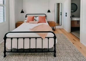 Een slaapkamer met een bed, nachtkastjes, een spiegel en uitzicht op de badkamer.