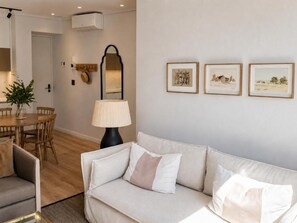 Een woonkamer met een bank, een eettafel, stoelen, een lamp en ingelijste foto's aan de wand.