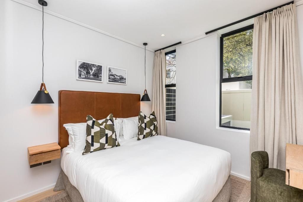 Quarto com uma cama grande, mesa de cabeceira de madeira, uma cadeira verde e janela com cortinas.