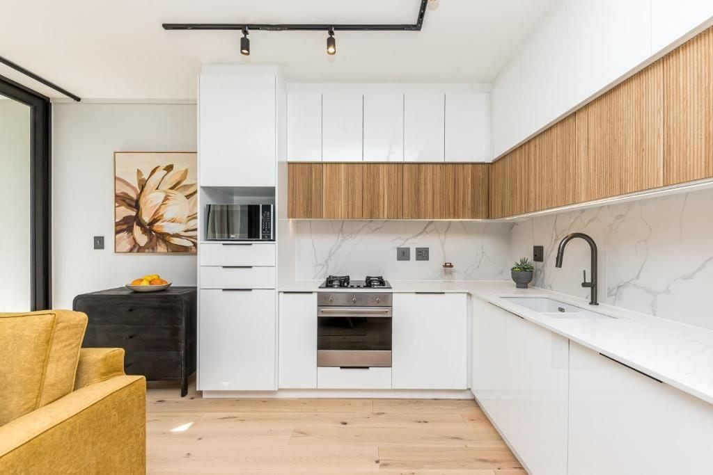 A modern kitchen with white cabinetry, a wooden accent wall, a black countertop, and a single stove.