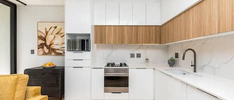 Una cocina moderna con armarios blancos, una pared decorativa de madera, una encimera negra y una sola estufa.
