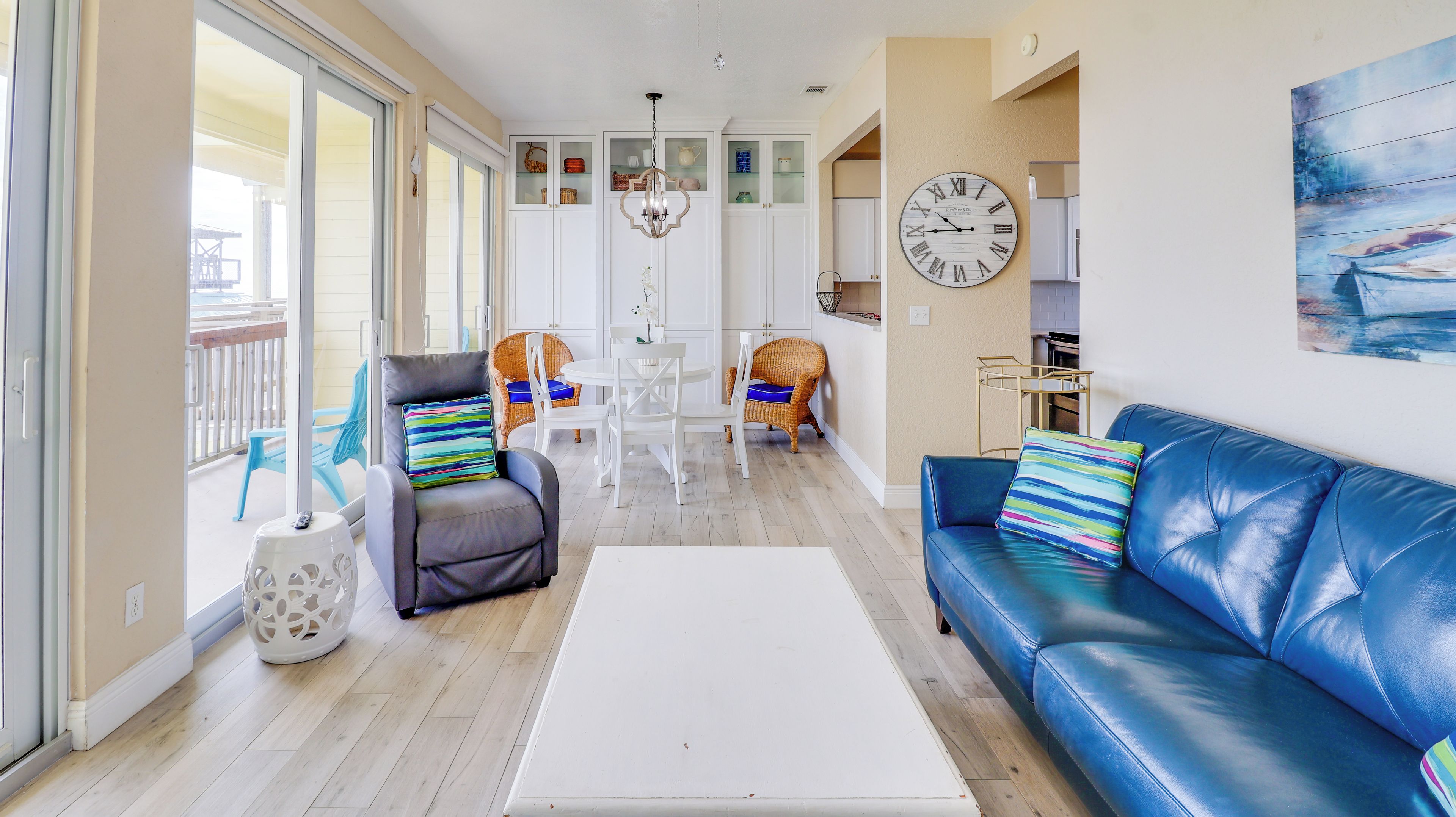 A modern living room with a blue leather sofa, a white coffee table, and a dining area with wicker chairs.