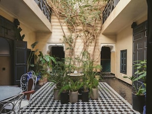 A courtyard with a checkered floor, potted plants, a table with chairs, and a staircase. - Riad El Aaiun (Marrakech)