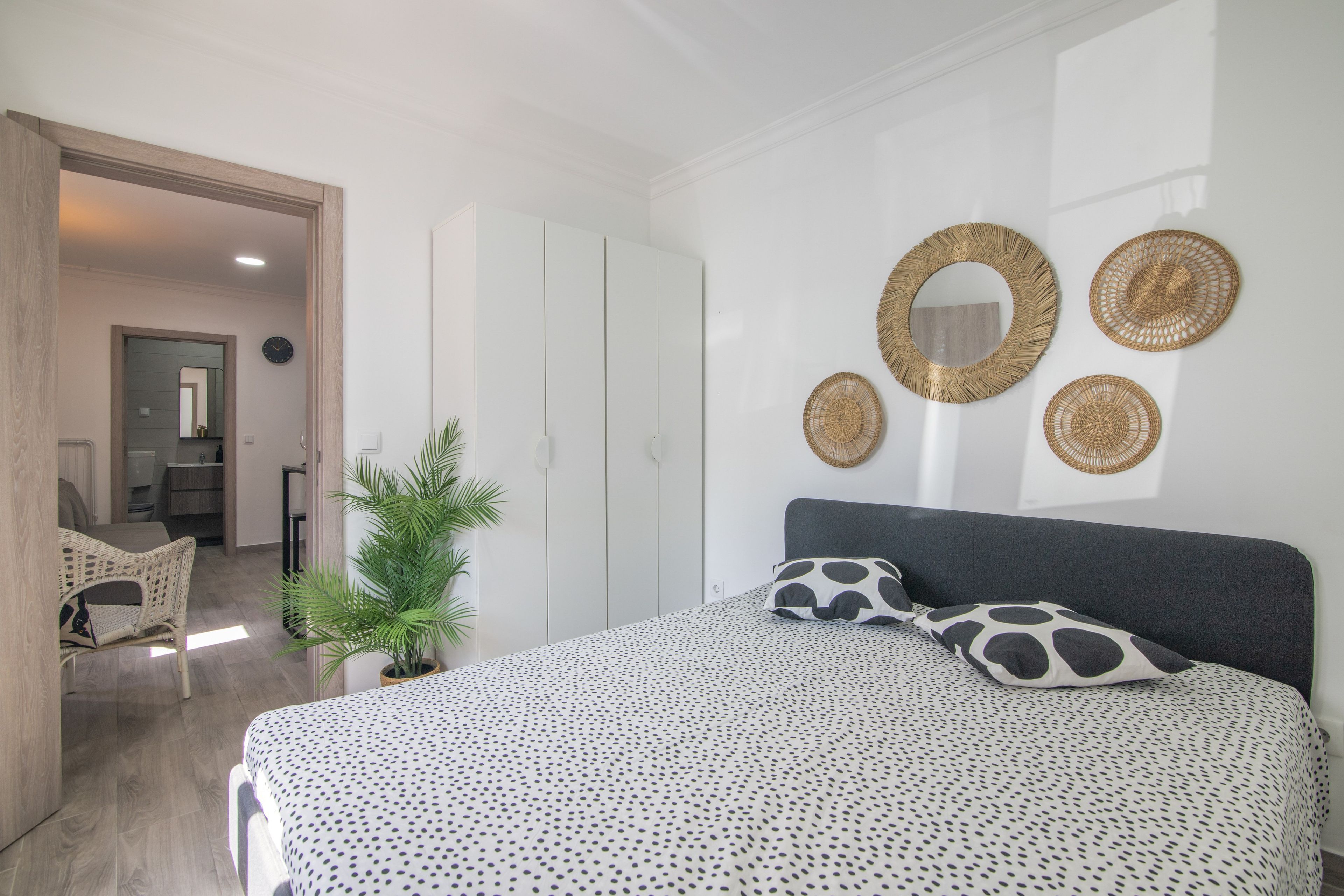 A bedroom with a bed, a potted plant, and decorative wall hangings.
