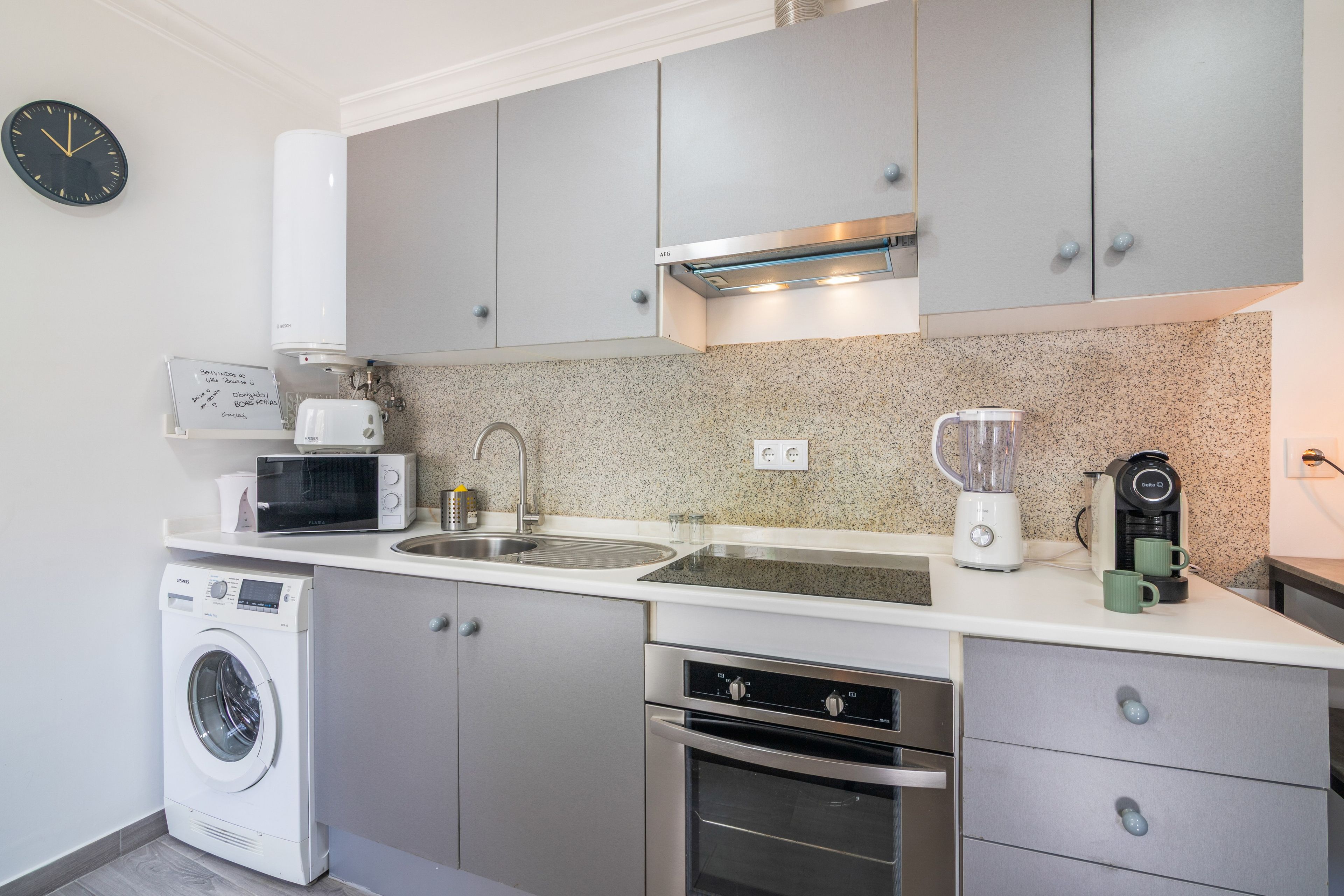 A compact kitchen with a washing machine, microwave, sink, and a coffee maker.